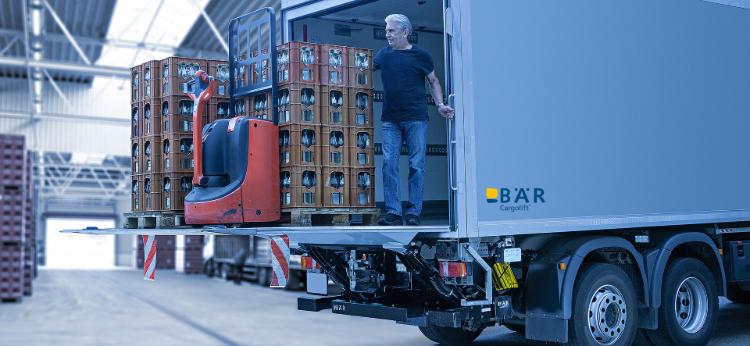 Řidič nákladního automobilu vykládá v hale nápoje a elektrický paletový vozík a hydraulická zdvihací plošina BAR.