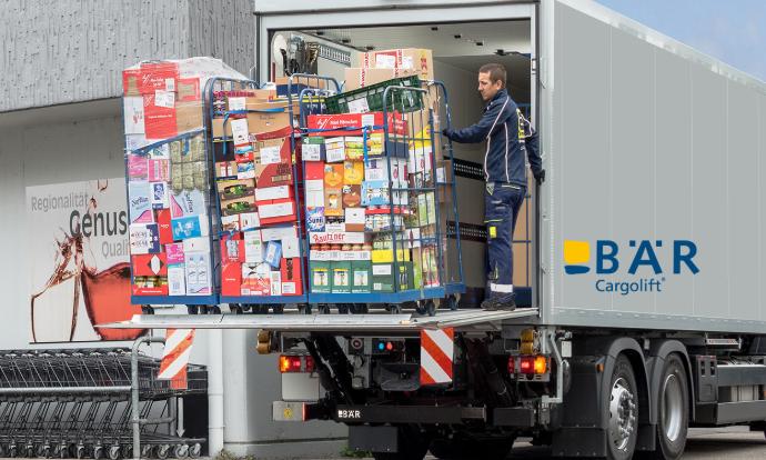 Řidič nákladního vozu nakládá před obchodem s potravinami z nákladního vozu několik kontejnerů na potraviny v rolích pomocí vozíku Bar Cargolift.