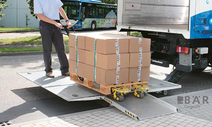 Řidič vjíždí na hydraulickou zdvihací plošinu Bar přes nájezdový můstek na chodníku.