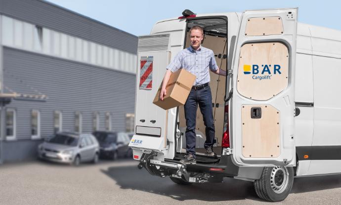 Muž vystupuje z dodávky zadními dveřmi s balíčkem, zatímco Bar VanLift FreeAccess zůstává nehybný.